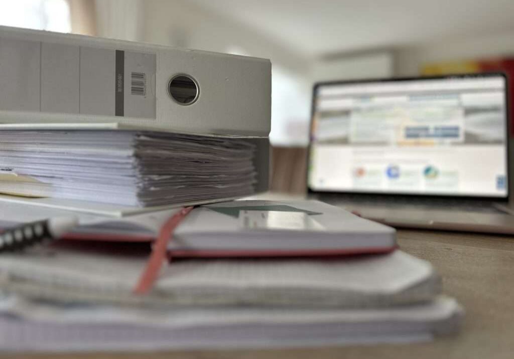 IMG_5685 Versicherung zahlt nicht bei Wasserschaden? Wasserschaden wer zahlt? Tisch mit vielen Akten und Unterlagen, in Hintergrund Laptop mit Wasserschadenshilfe.de WDS Website geöffnet.